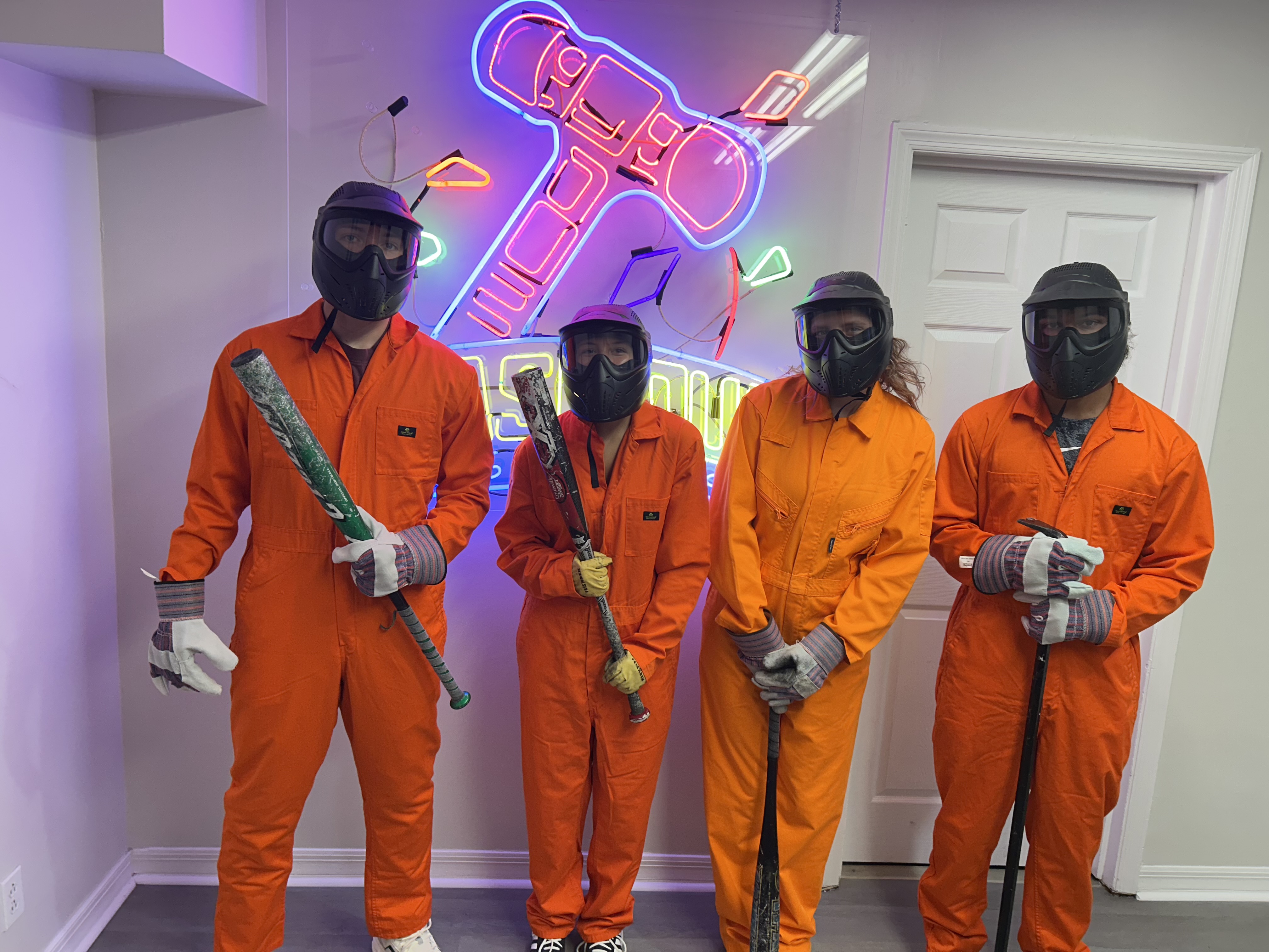 Crash Out Rage Rooms customers in orange jumpsuits selecting baseball bats from a barrel of smash tools before their session