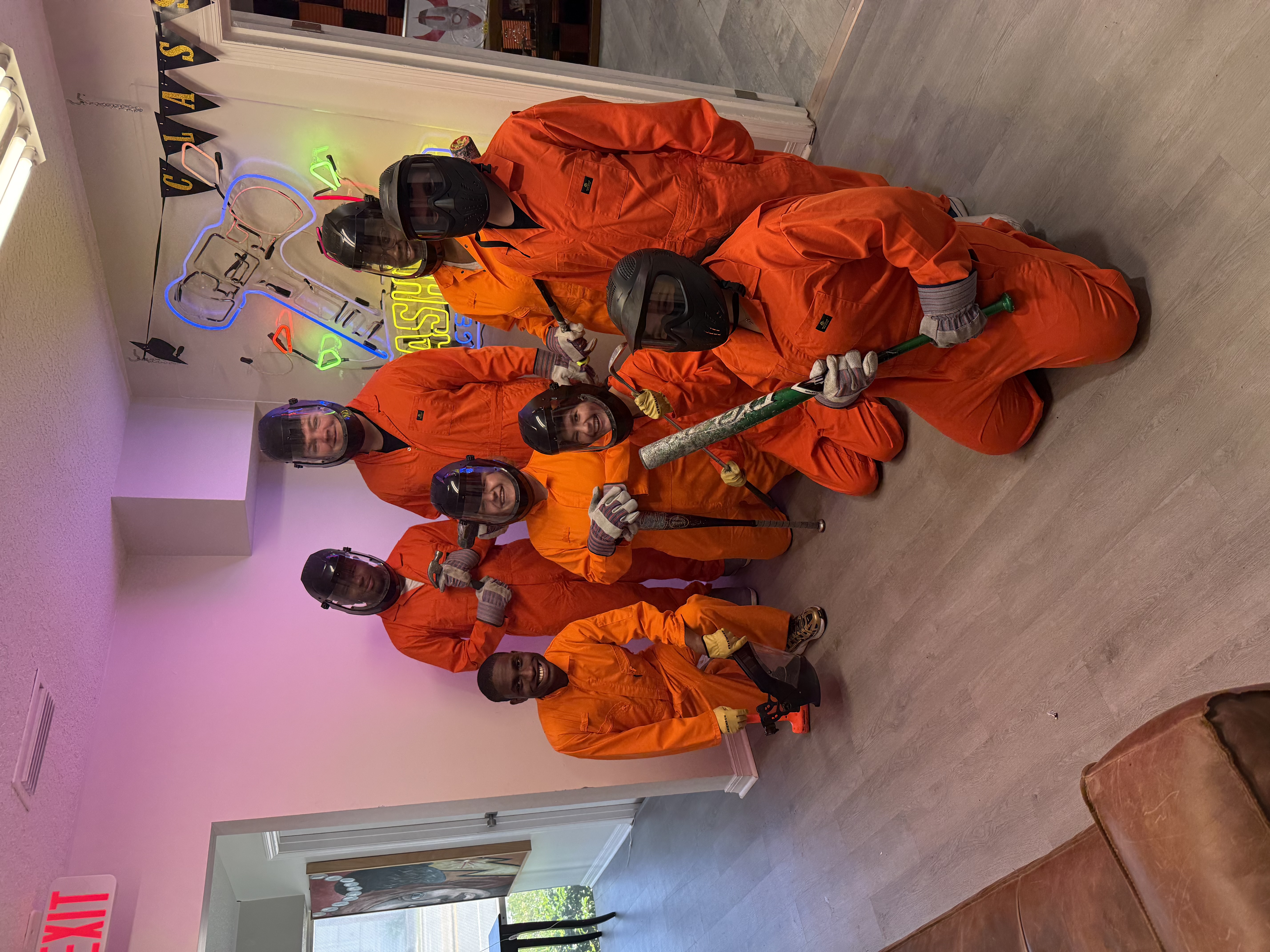 Eight Crash Out customers in orange protective gear posing together before a smash room session