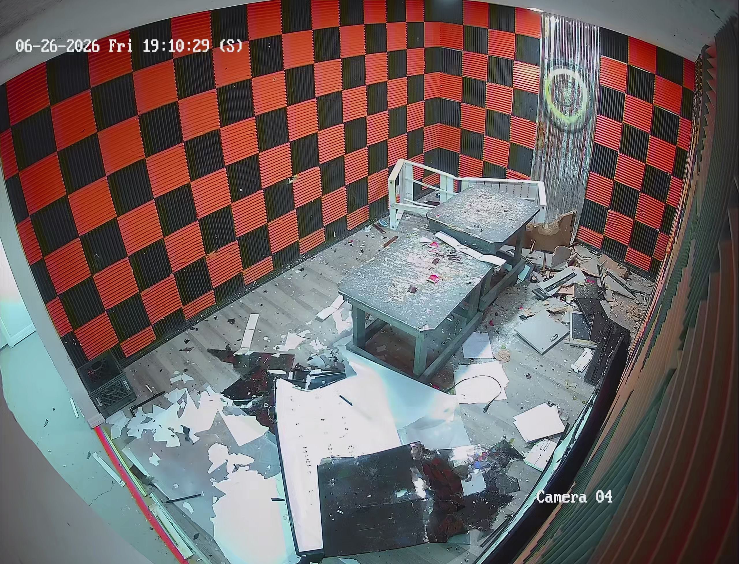 Security camera view of fully demolished Crash Out rage room after a session — broken screens, shattered glass, and debris on the floor