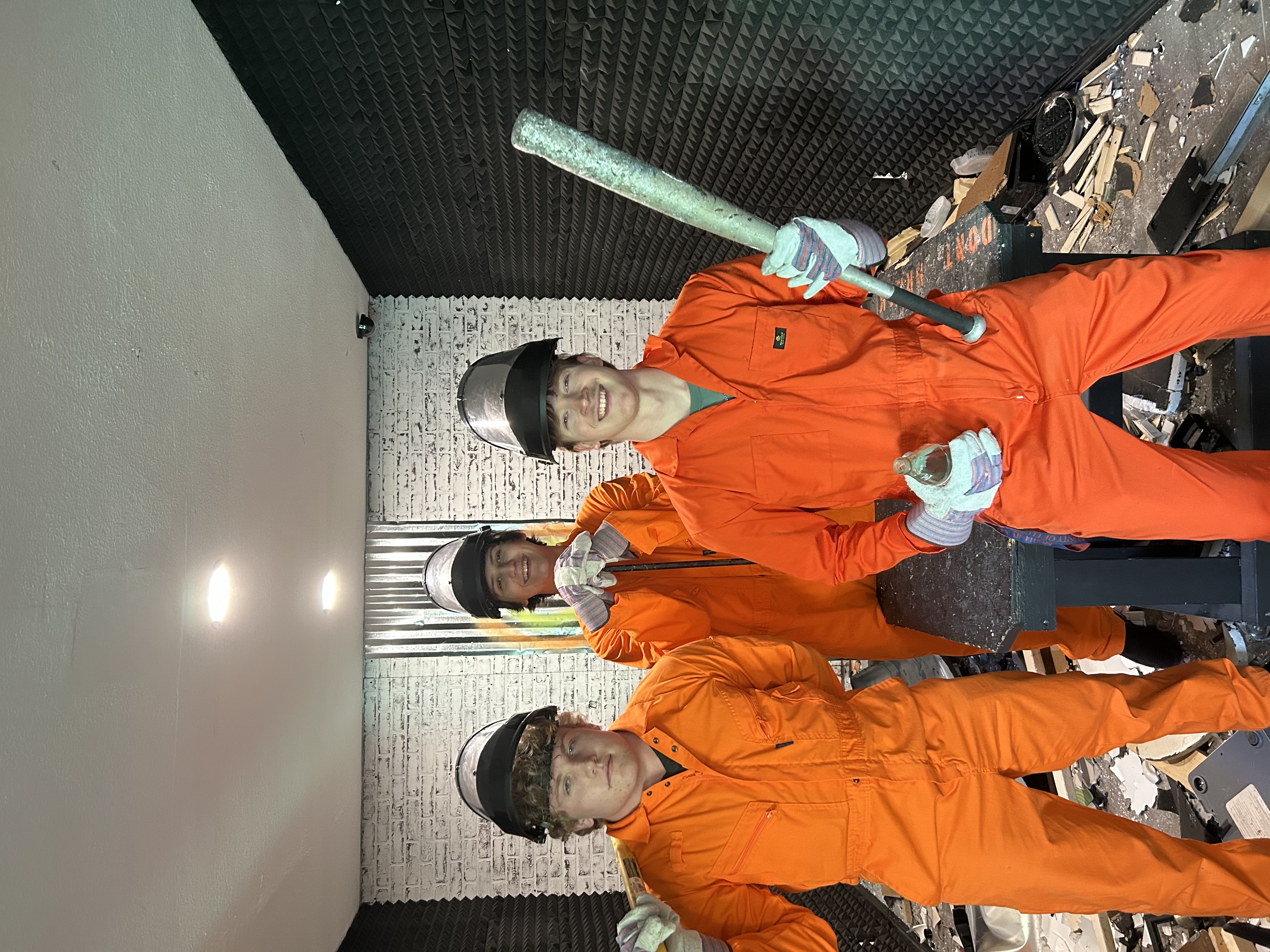 Three Crash Out guests celebrating after a smash room session surrounded by broken electronics